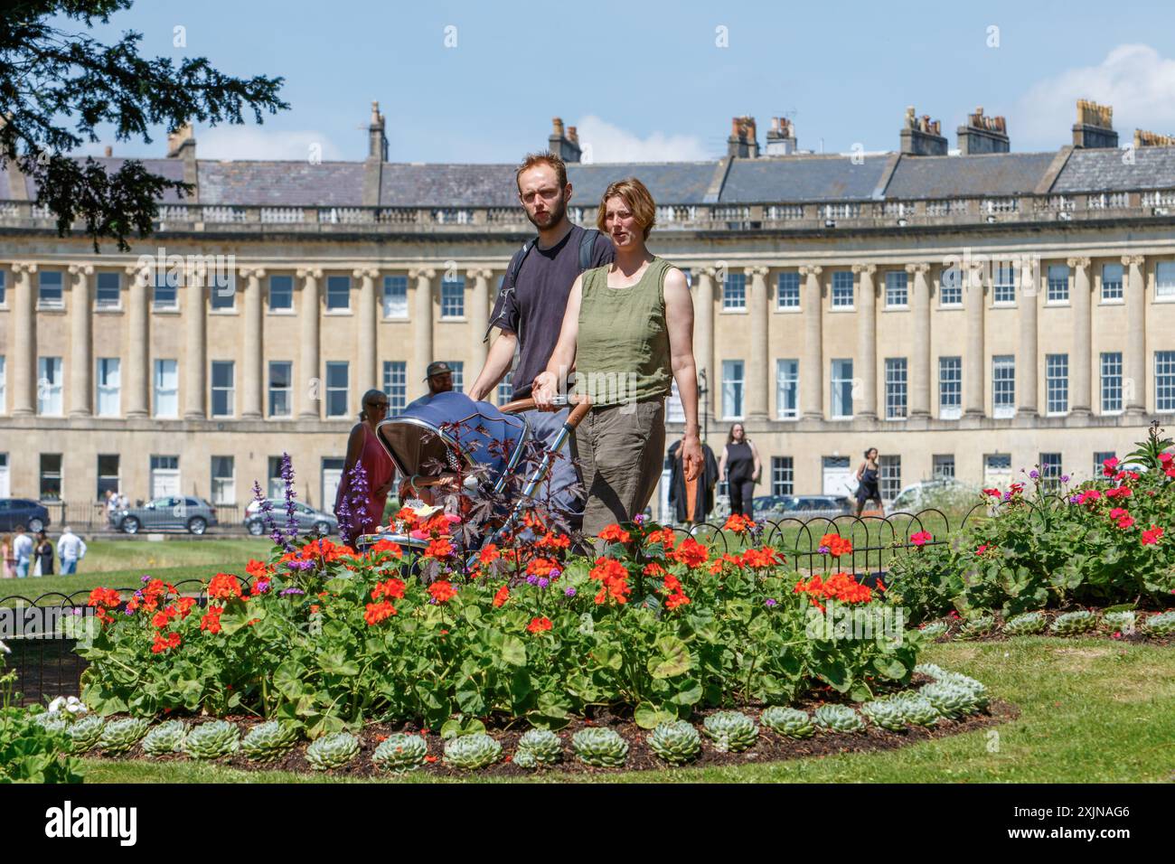 Bath, Großbritannien, 19. Juli 2024. In vielen Teilen Englands und Wales herrschen warme Temperaturen von 31 °C. der weltberühmte Royal Crescent im Hinterland ist zu sehen, wie die Menschen das sehr warme Wetter genießen und an bunten Blumen im Royal Victoria Park vorbeilaufen. Quelle: Lynchpics/Alamy Live News Stockfoto