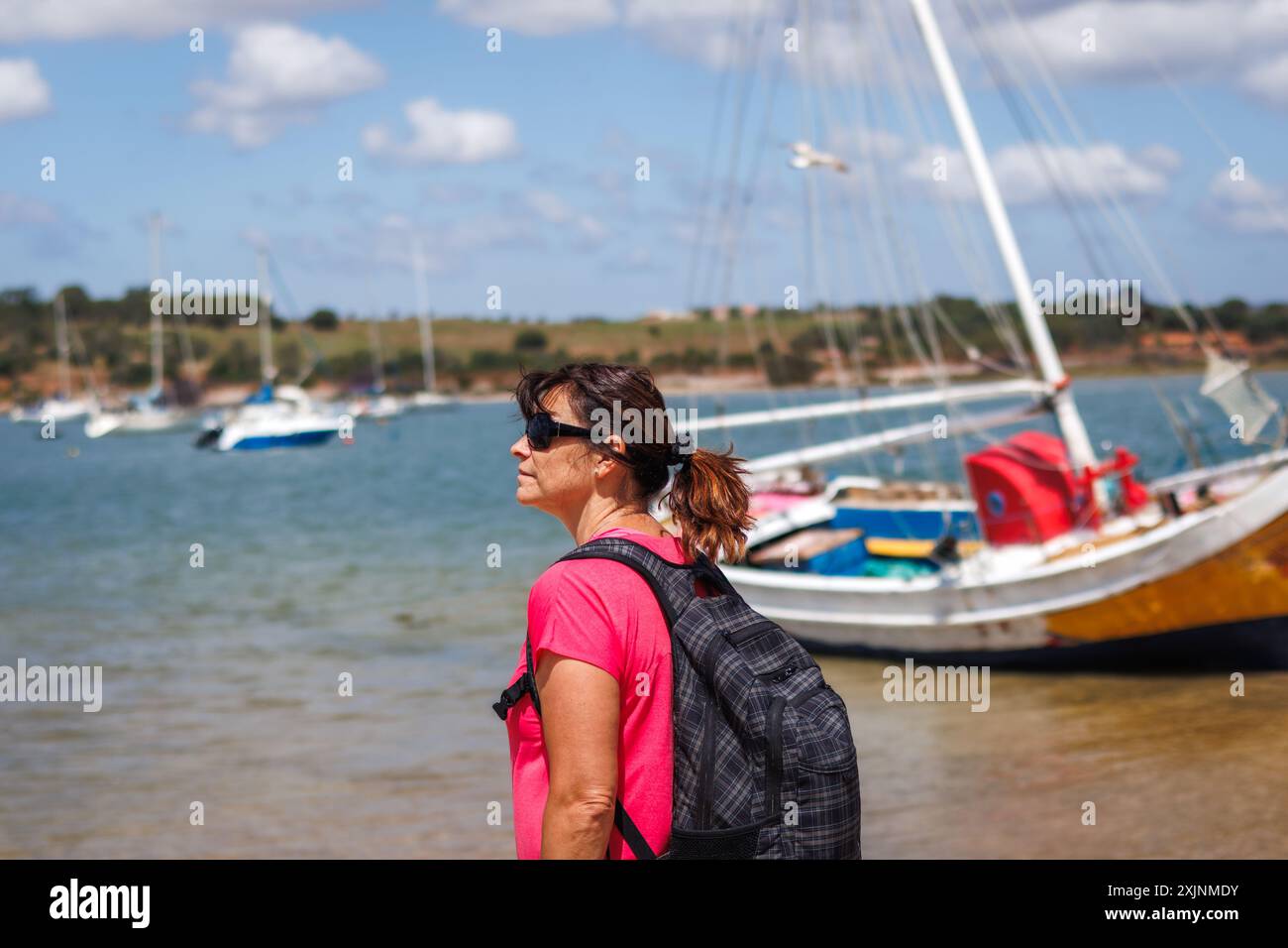 Frau, die beim Wandern am Meer im typischen Dorf Alvor in der Algarve, Portugal, steht. Fischerboote, die in einem Hafen auf dem Meer ankern Stockfoto