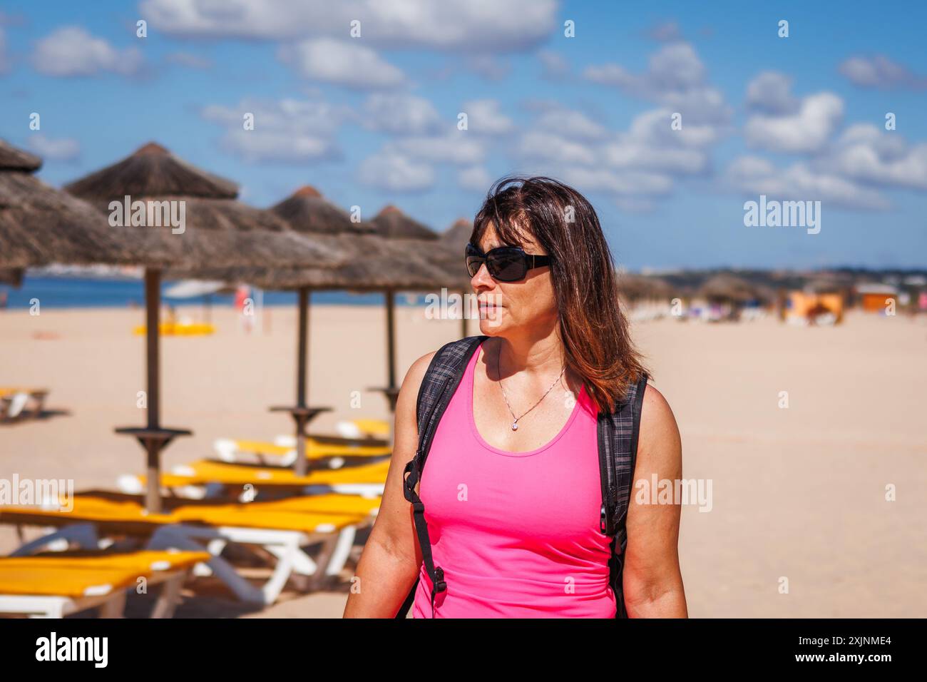 Badeurlaub in der Algarve, Portugal. Eine fitte und vitale reife Frau wählt Liegestühle mit Sonnenschirm zum Entspannen am Strand. Sommerurlaub Stockfoto