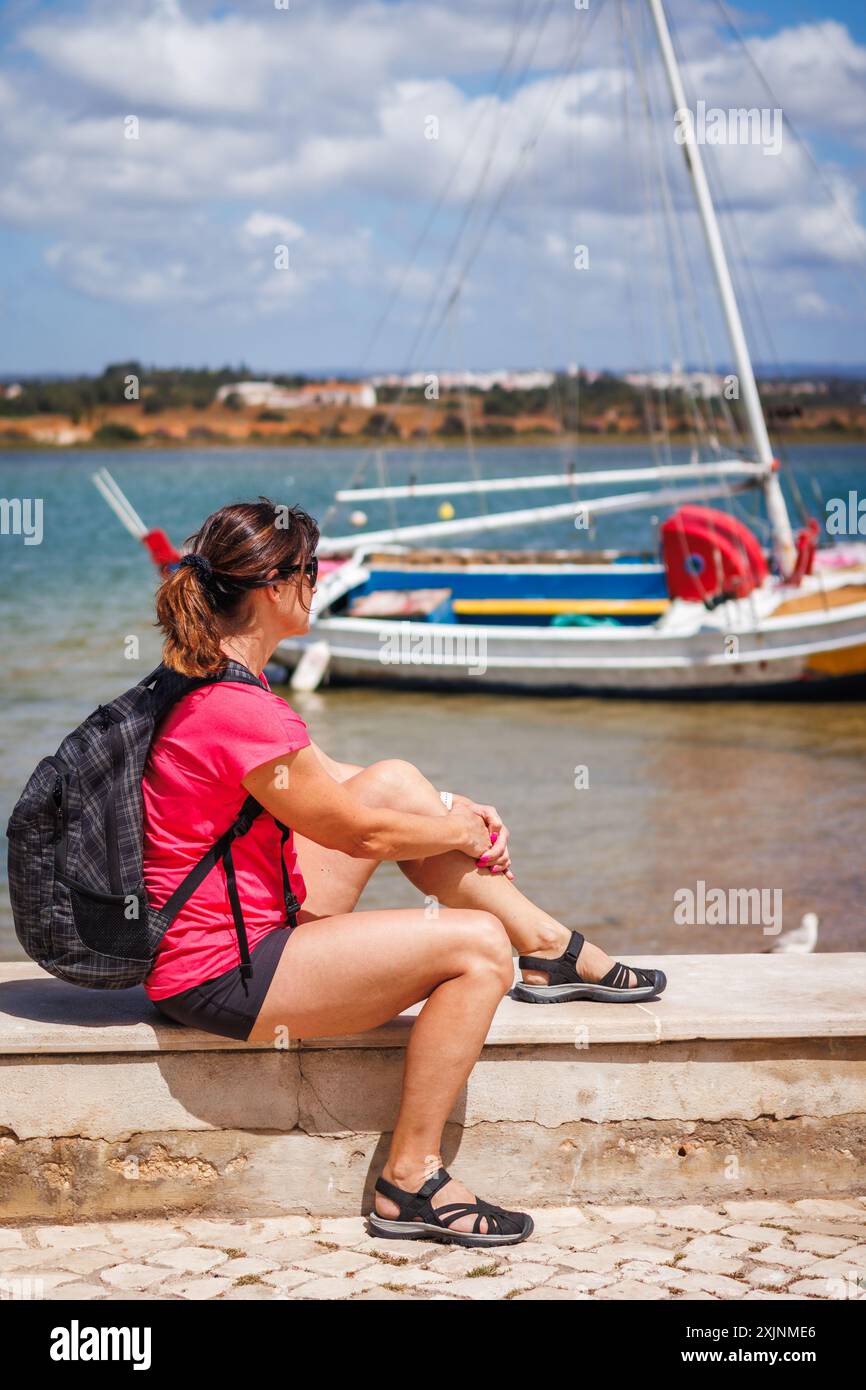 Frau, die sich ausruht und auf der Suche nach einem Boot an der Küste während einer Wanderung im typischen Fischerdorf Alvor in der Algarve, Portugal Stockfoto