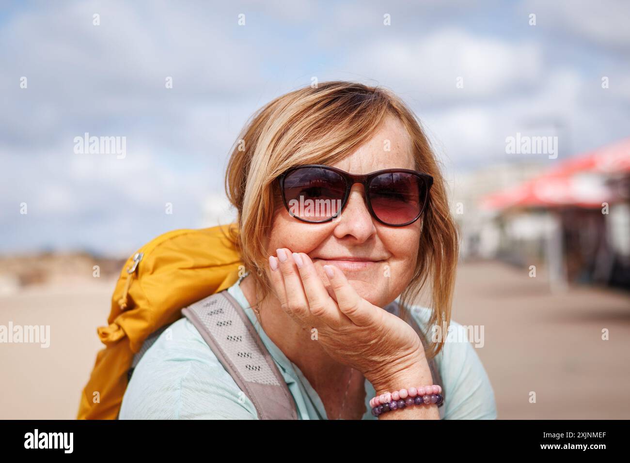 Porträt einer glücklichen, lächelnden Reifen-Touristin mit Sonnenbrille und Rucksack, die sich am Strand während einer Wanderung entlang der Küste in der Algarve, Portugal, entspannt Stockfoto