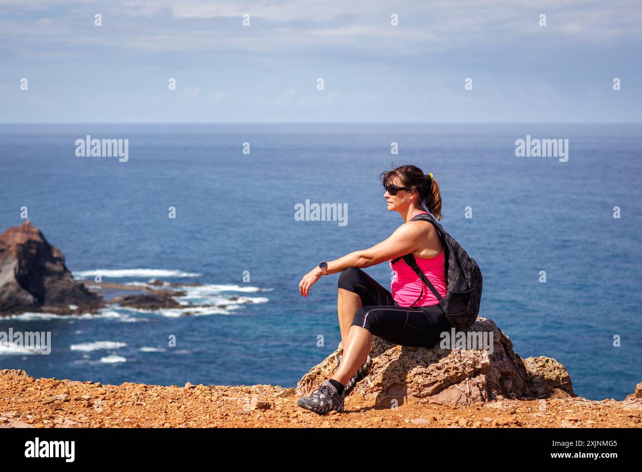 Sportliche reife Frau, die beim Wandern an der Algarve ausruht. Wanderer genießen den Blick auf den Atlantischen Ozean von der Klippe in Portugal Stockfoto