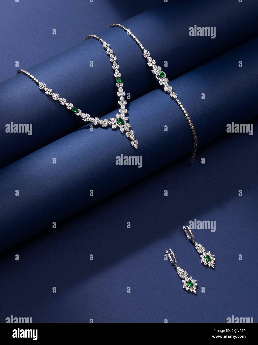 Elegantes Schmuckset mit grünen Edelsteinen und Diamanten auf dunkelblauem Hintergrund. Stockfoto
