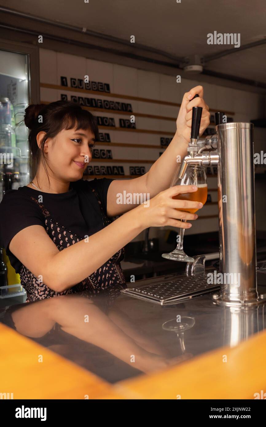 Profilporträt einer Kellnerin, die ein Glas Bier aus dem Zapfhahn füllt. Stockfoto