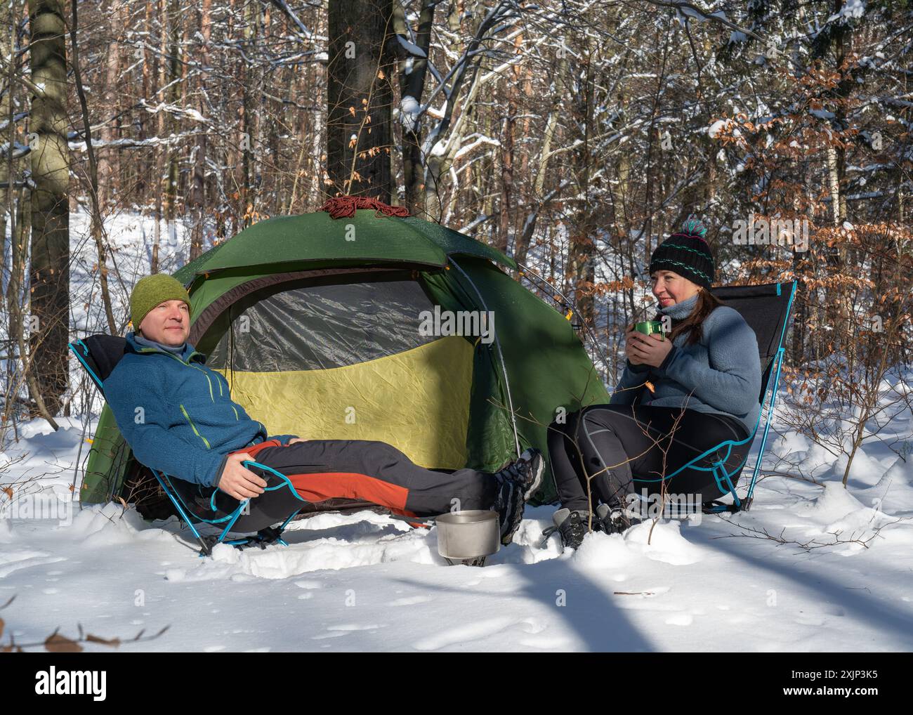 Ein Mann und eine Frau bereiten Tee und Essen in der Nähe eines Zeltes in einem verschneiten Wald zu. Liebe. Winter. Romantik. Aktiver Lebensstil. Glück. Freude. Extrem. Kalt. Der Klagegrund Stockfoto