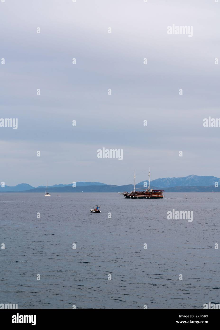 Ein altes Holzboot mit vielen Touristen an Bord in der Adria. Es ist Abend. Hohe Berge am Horizont. Kleine Yachten und Boote segeln in der Nähe. C Stockfoto