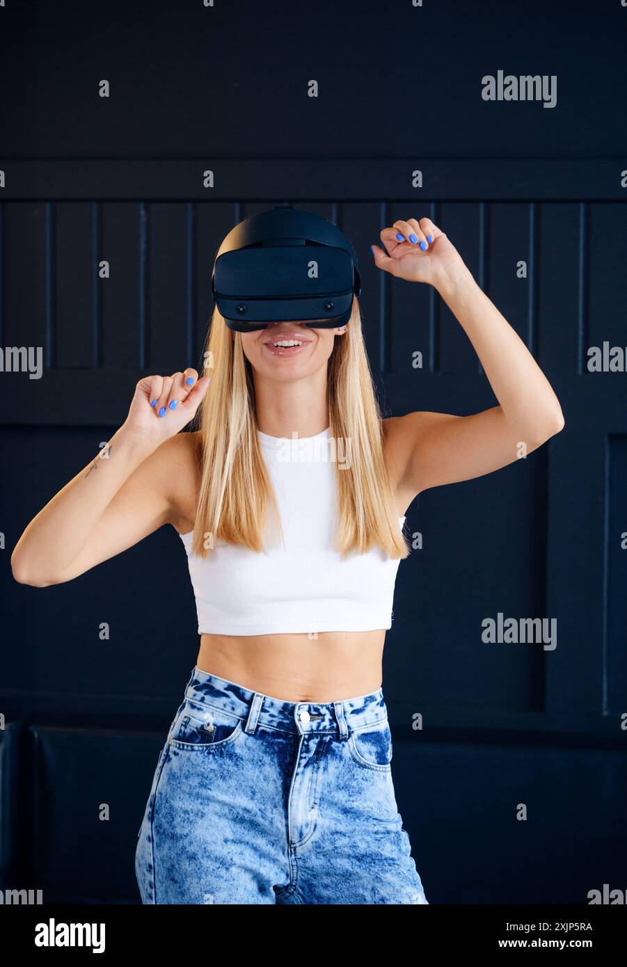 Yong-Frau, die ein Virtual-Reality-Headset trägt, lächelt, während sie vor einem dunklen Hintergrund tanzt. VR und digitale Welt Stockfoto