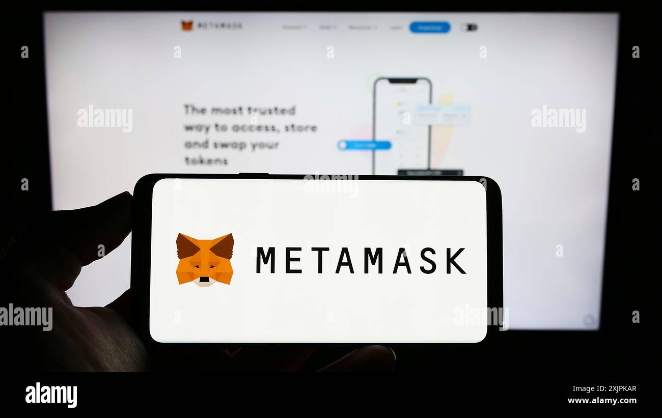 Stuttgart, Deutschland, 07.11.2023: Person, die ein Mobiltelefon mit dem Logo der Kryptowährungs-Wallet-Software MetaMask auf dem Bildschirm vor der Unternehmenswebseite hält. Stockfoto