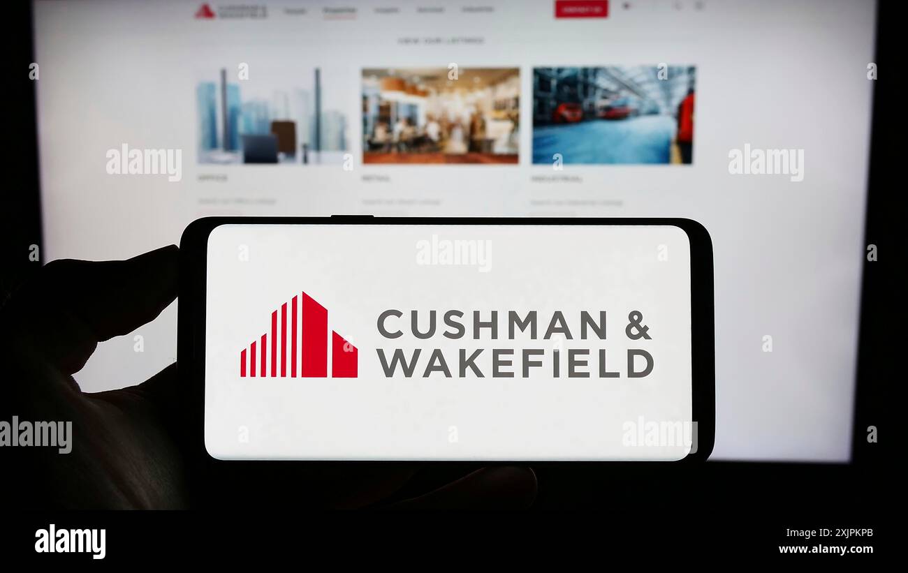 Stuttgart, 15.07.2023: Person, die ein Mobiltelefon mit dem Logo der Immobilienfirma Cushman Wakefield plc vor dem Geschäft auf dem Bildschirm hält Stockfoto