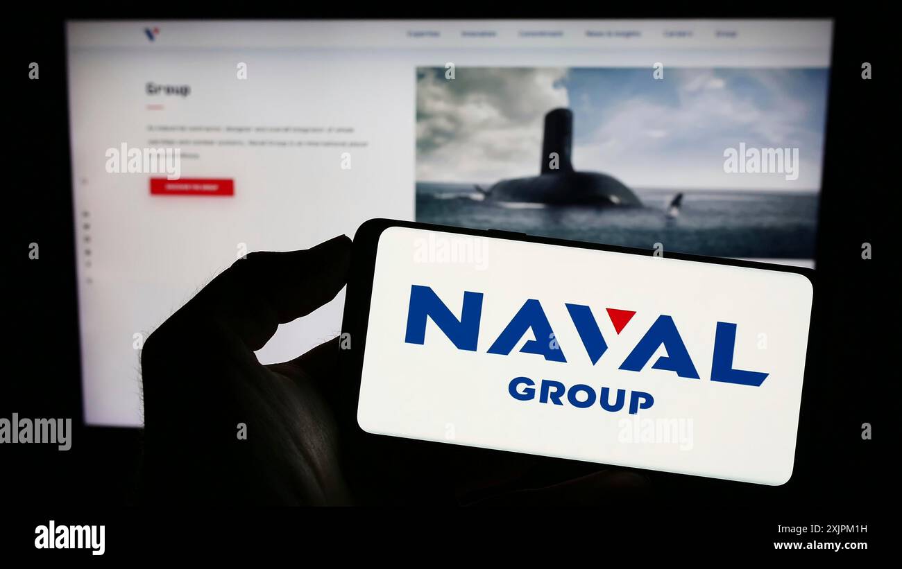 Stuttgart, 15.07.2023: Person, die ein Mobiltelefon mit dem Logo des französischen Verteidigungsunternehmens Naval Group SA auf dem Bildschirm vor dem Business Web hält Stockfoto