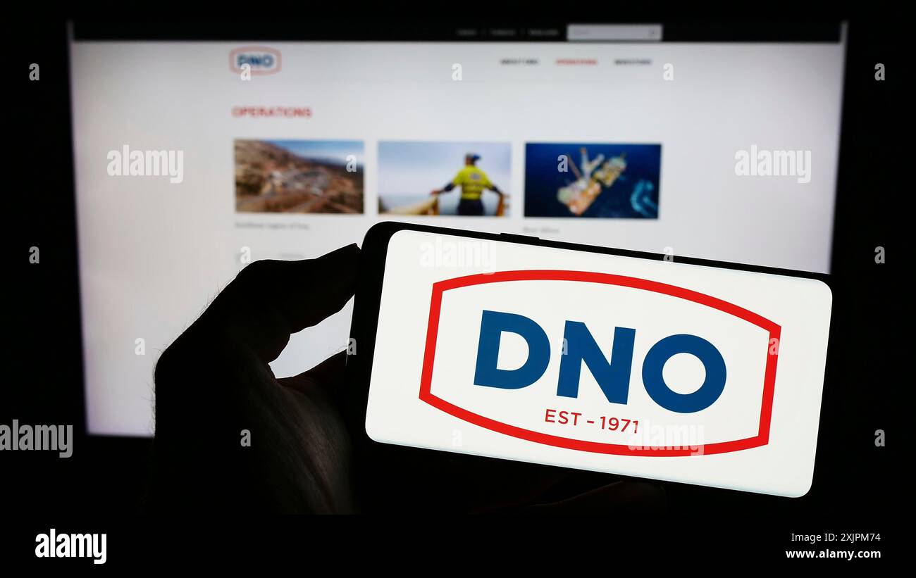 Stuttgart, Deutschland, 21.07.2023: Person, die ein Mobiltelefon mit dem Logo des norwegischen Öl- und Gasunternehmens DNO ASA auf dem Bildschirm vor der Webseite der Firma hält. Stockfoto