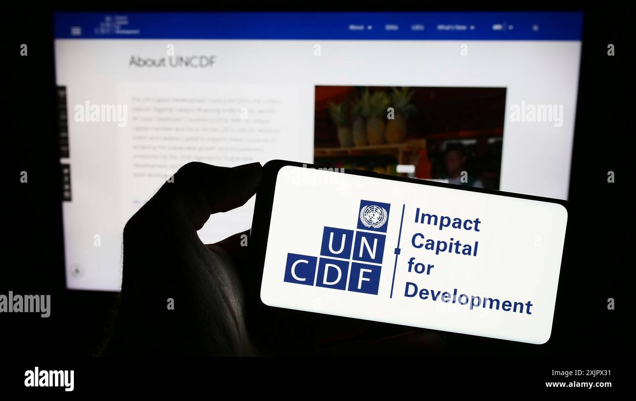 Stuttgart, Deutschland, 25.09.2023: Person, die ein Mobiltelefon mit dem Logo des Fonds der Vereinten Nationen für Kapitalentwicklung (UNCDF) vor der Webseite hält. Fokus Stockfoto