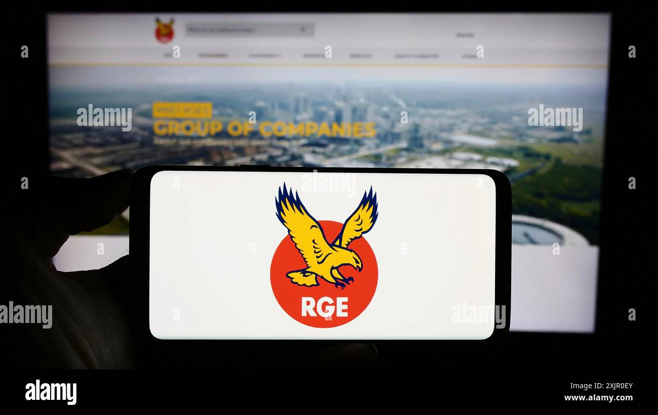 Stuttgart, Deutschland, 11.08.2023: Person, die ein Mobiltelefon mit dem Logo der singapurischen Firma Royal Golden Eagle (RGE) vor der Webseite hält. Stockfoto