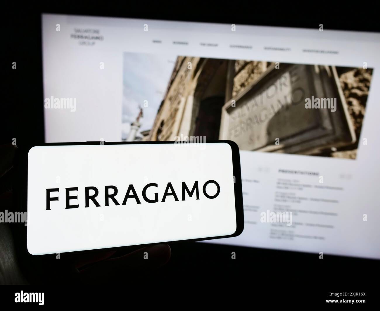 Stuttgart, 16.11.2023: Person, die ein Mobiltelefon mit Logo des italienischen Modeunternehmens Salvataore Ferragamo S.p.A. vor dem Geschäft hält Stockfoto