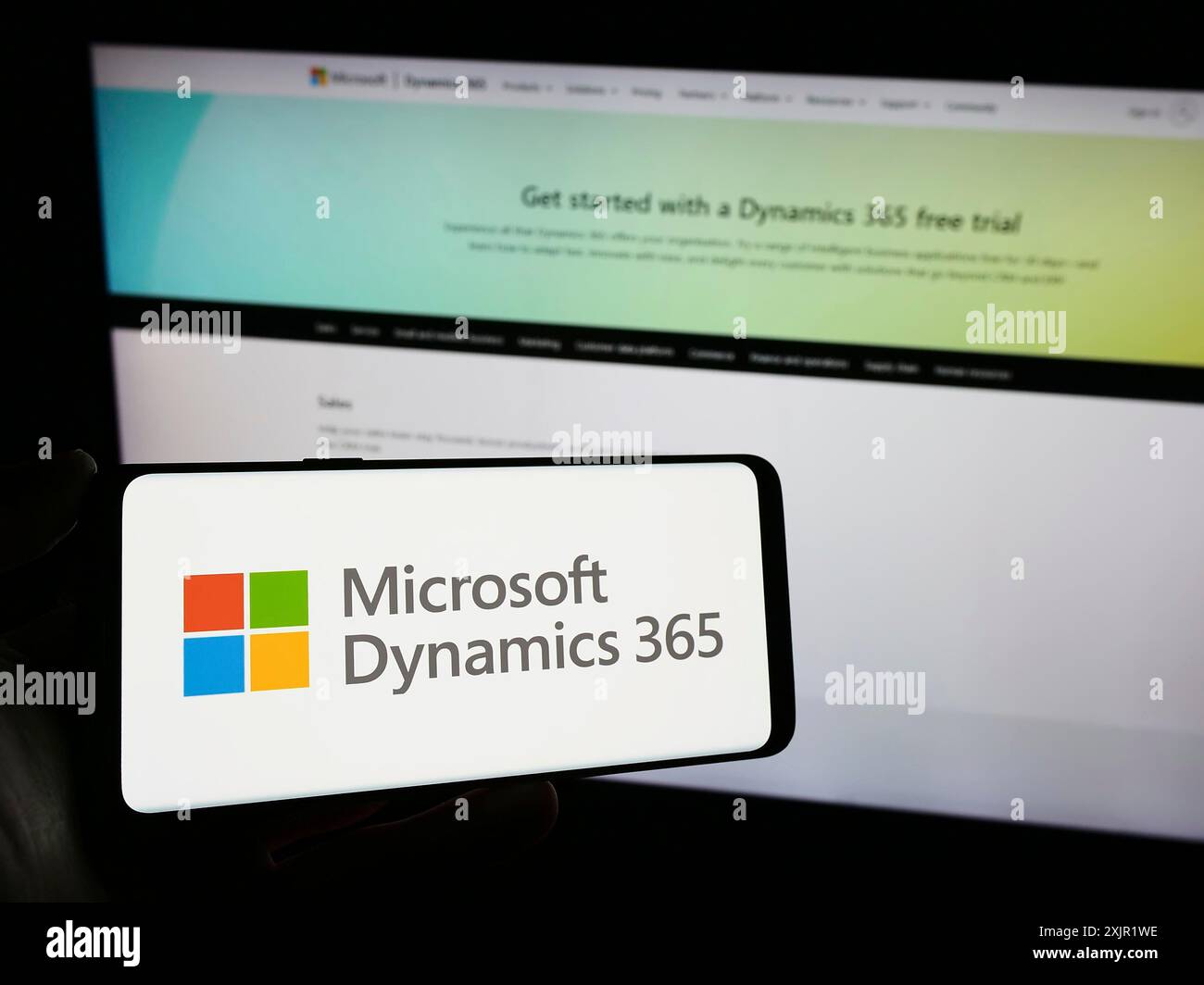 Stuttgart, 27.11.2023: Person, die ein Mobiltelefon mit dem Logo des Buchhaltungssoftwareprodukts Microsoft Dynamics 365 vor dem Business Web hält Stockfoto