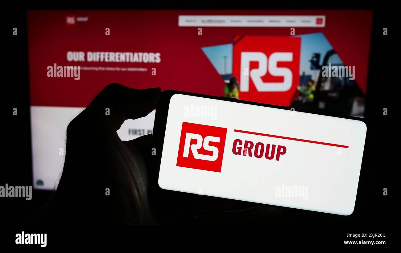 Stuttgart, 24.11.2023: Person, die ein Mobiltelefon mit Logo des britischen Stromverteilers RS Group plc vor dem Geschäft hält Stockfoto