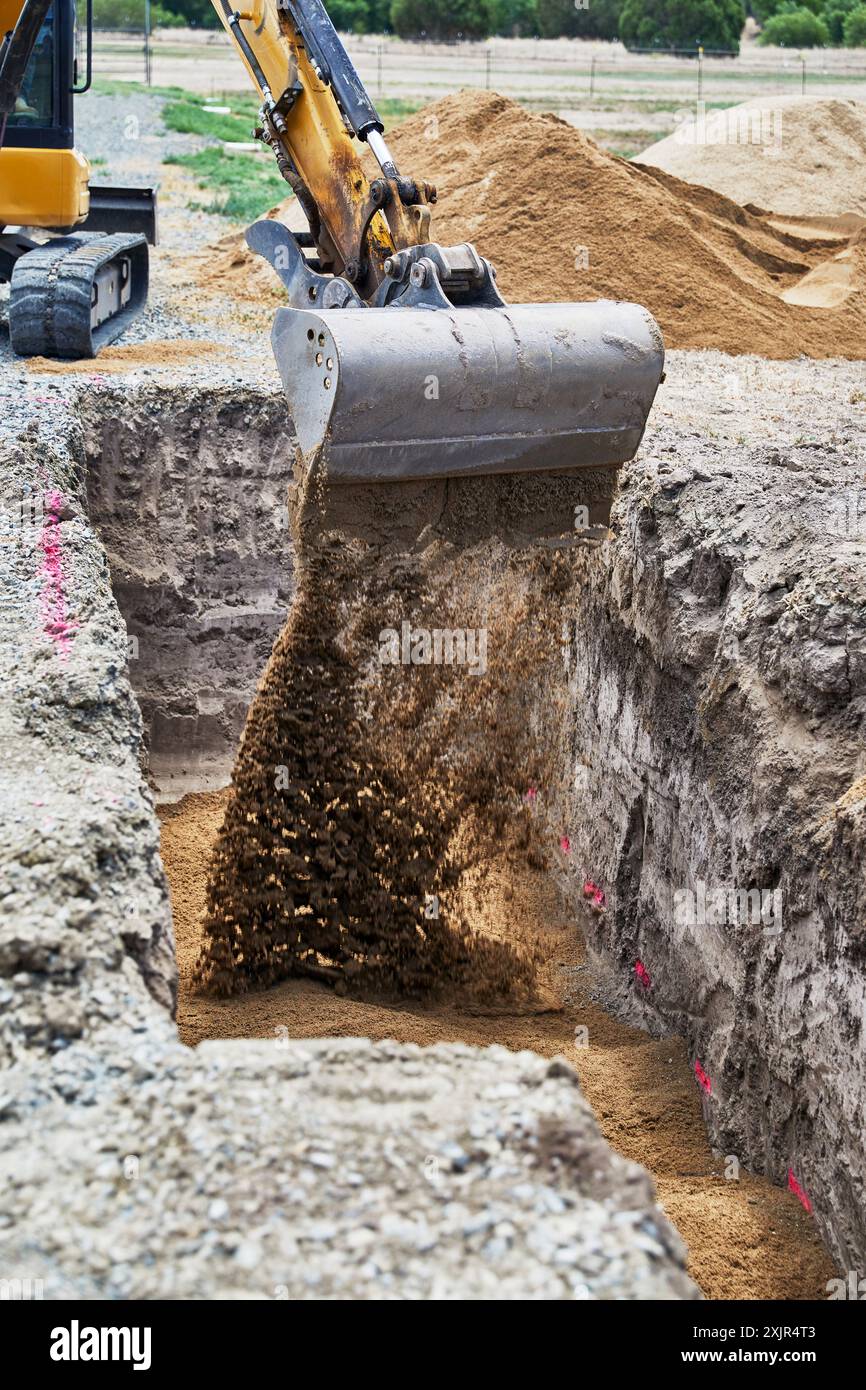 Mini-Löffel aus Stahl auf dem Arm eines Baggers, der Sand in ein tiefes Loch bringt, um einen vergrabenen Propangentank vorzubereiten Stockfoto