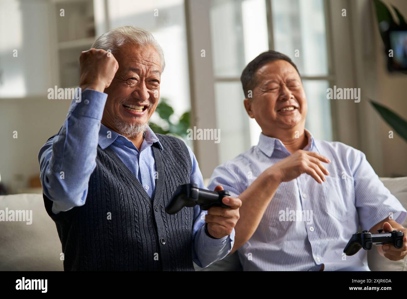 Zwei glückliche ältere asiatische Männer sitzen zu Hause auf der Couch und spielen Videospiele Stockfoto