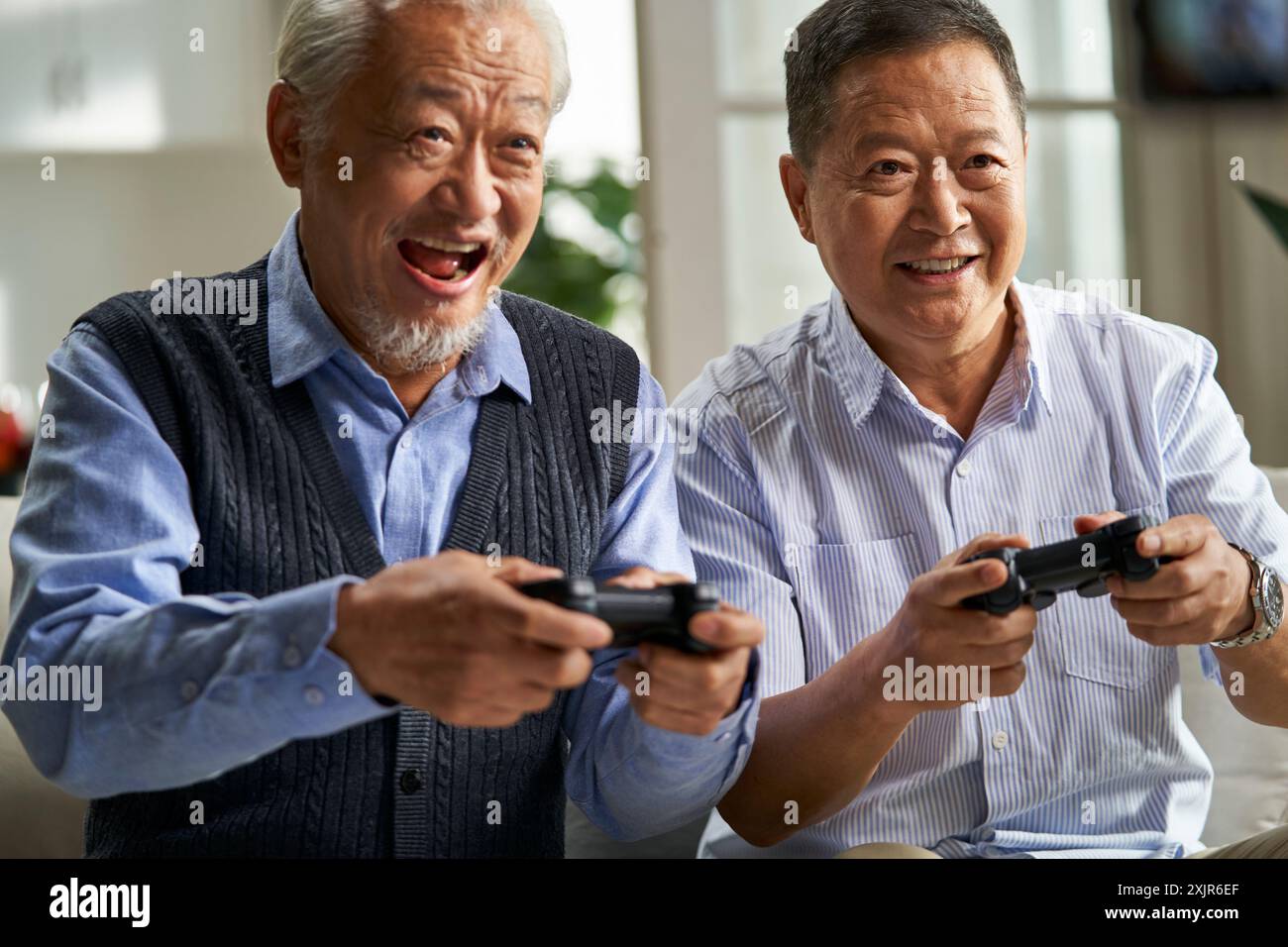 Zwei glückliche ältere asiatische Männer sitzen zu Hause auf der Couch und spielen Videospiele Stockfoto