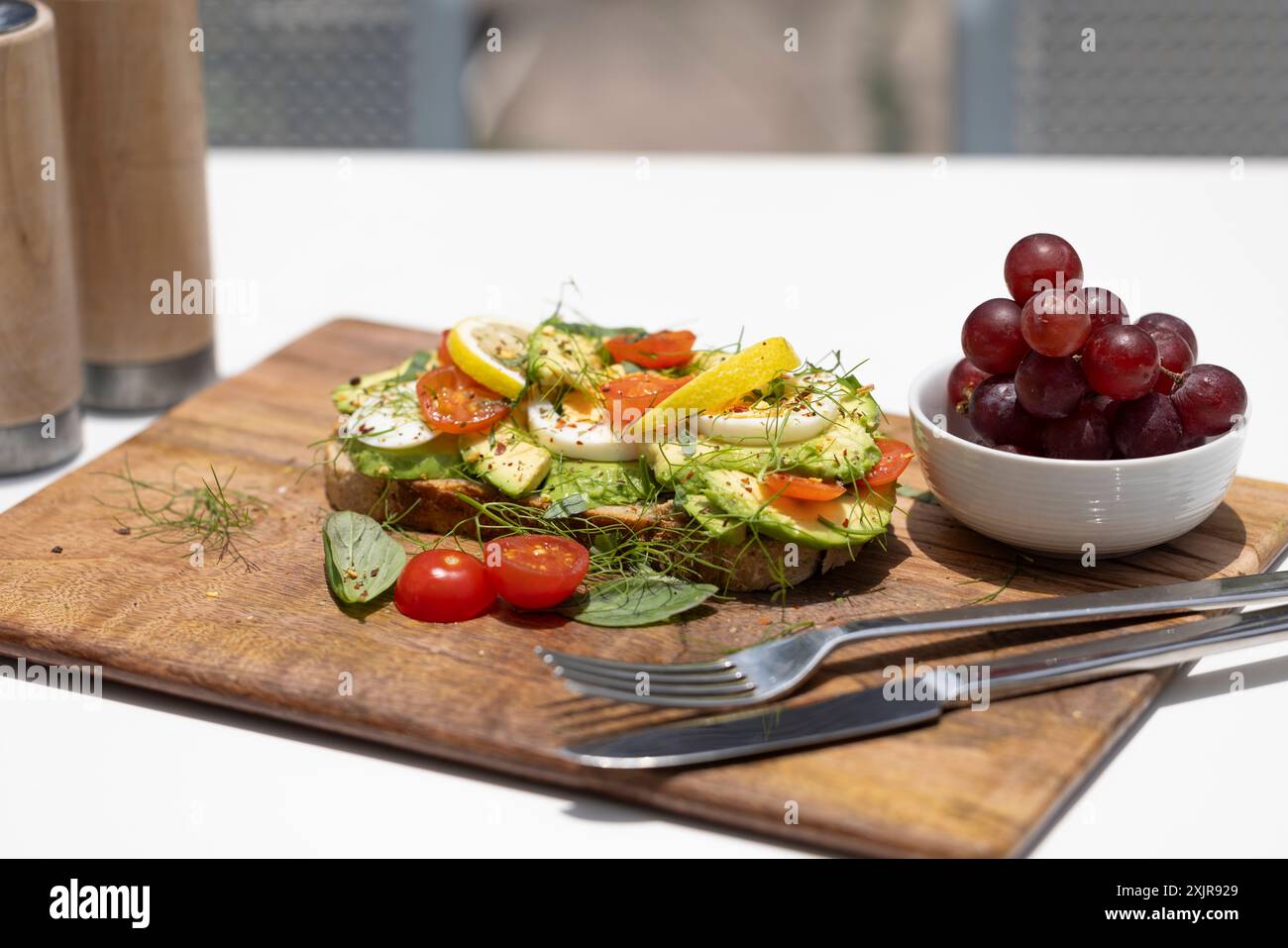Ein köstlicher Frühstücksteller mit pochierten Eiern, Avocado-Toast mit Zitrone und Tomate, einem frischen Salat und einem kleinen Traubenstrauß. Stockfoto