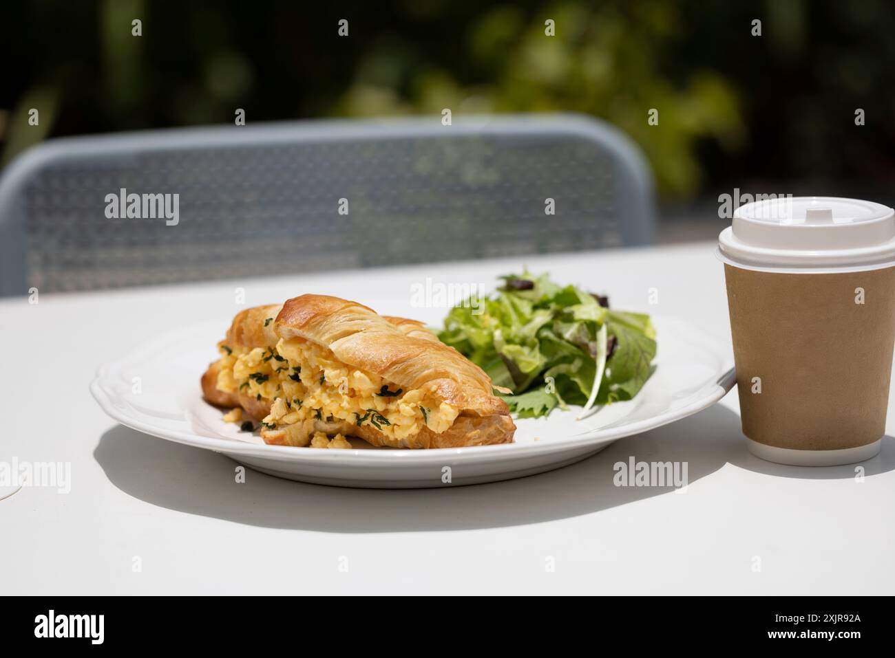 Ein Frühstücksangebot mit einem Croissant mit Rührei und Kräutern, serviert mit einem Salat auf einem weißen Teller. Stockfoto