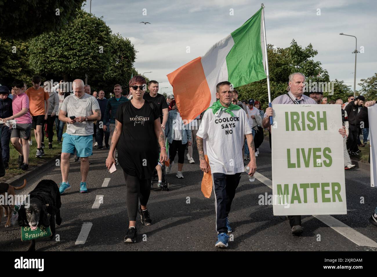 Demonstranten marschieren mit Fahnen und der irischen Flagge während der Demonstration. Ein zweiter Protest fand am Freitagabend in Coolock im Norden von Dublin statt. Die Menschen protestieren weiterhin gegen die Wiedereröffnung der ehemaligen Crown Paintanlage, in der Migranten untergebracht werden sollen, und gegen die Masseneinwanderung in Irland. Die Demonstranten, die vom Standort in Richtung Bahnhof Coolock Garda marschierten, beklagten sich auch über die Gewalt, die sie bei dem letzten Protest am 15. Juli erlitten hatten, und forderten die Regierung auf, ihrer Gemeinde mehr Aufmerksamkeit zu schenken. Der heutige Protest verlief friedlich Stockfoto