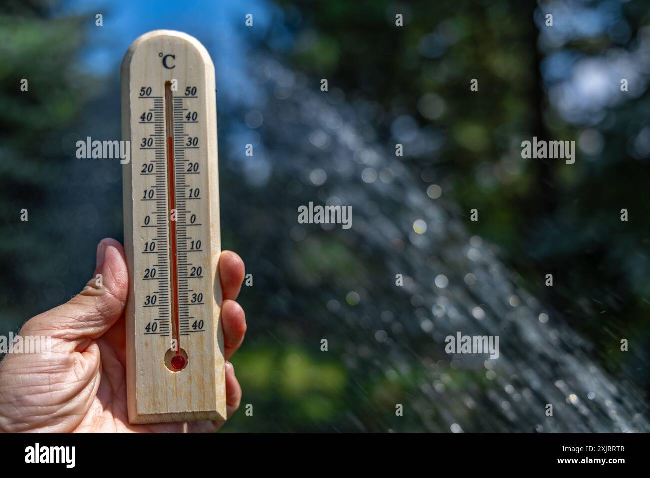 Ein Mann hält im Garten ein Holzthermometer in der Hand, das eine sehr hohe Temperatur anzeigt - Schutz vor Hitze Stockfoto