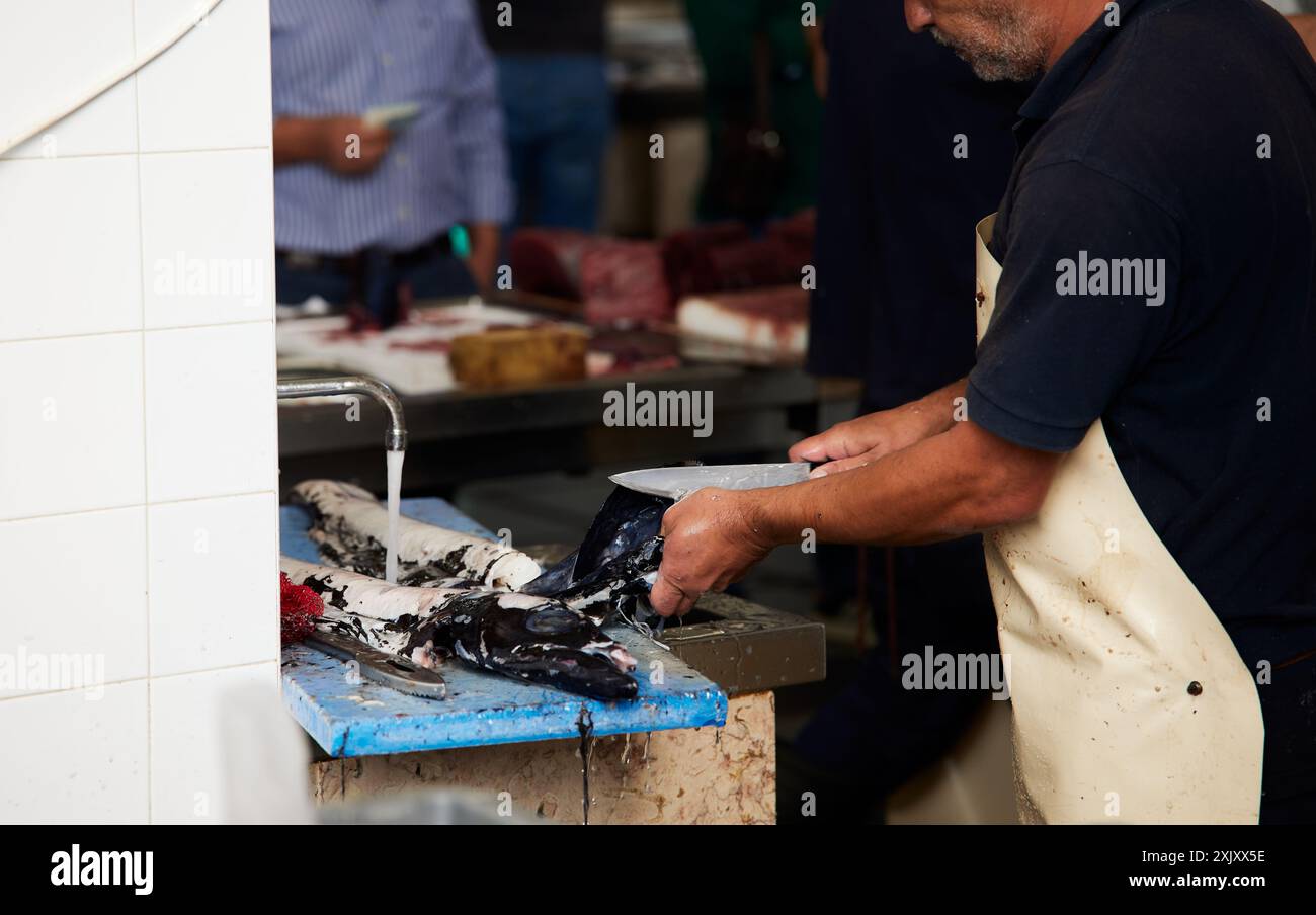 Ein Fischhändler putzt frischen Fisch an einem Marktstand mit einem Messer und fließendem Wasser in Funchal, Madeira, Portugal Stockfoto