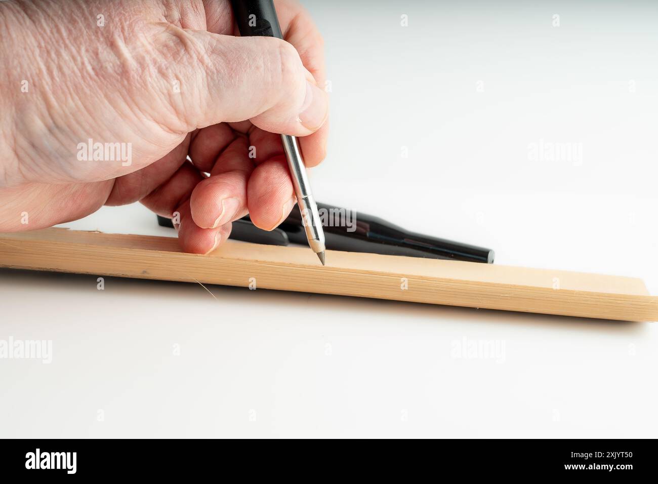Zimmermann markiert eine Holzdiele mit einem mechanischen Bleistift, der für die Holzbearbeitung verwendet wird, isoliert auf weißem Hintergrund Stockfoto