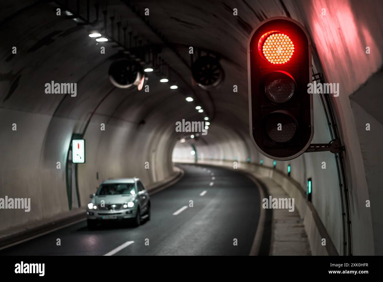 Ein weißes Auto fährt durch einen Tunnel mit einer roten Ampel, die von der Decke hängt. Stockfoto