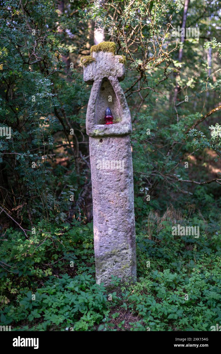 Ein Steinkreuz aus dem 16. Jahrhundert am Rande eines Waldes in Šipín, Tschechien. Die Kerzenlampe aus Glas steht in ihrer Nische. Stockfoto