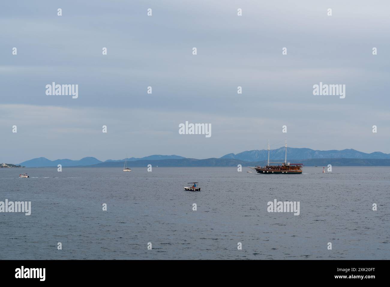 Ein altes Holzboot mit vielen Touristen an Bord in der Adria. Es ist Abend. Hohe Berge am Horizont. Kleine Yachten und Boote segeln in der Nähe. C Stockfoto