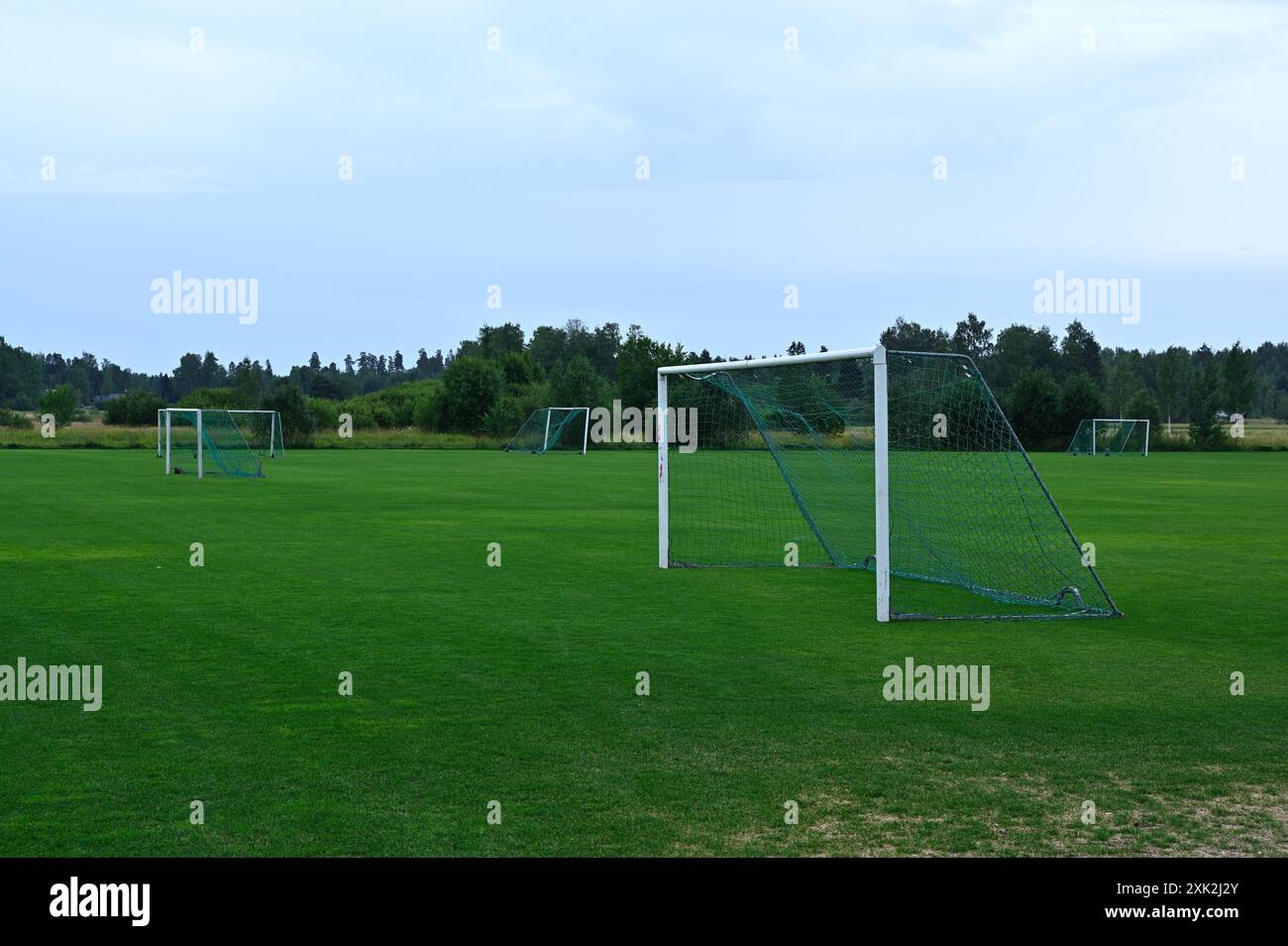 Ein leeres Fußballfeld mit mehreren Torpfosten vor einem Hintergrund von üppigem Grün und Bäumen unter einem bewölkten Himmel. Das gepflegte grüne Gras Stockfoto