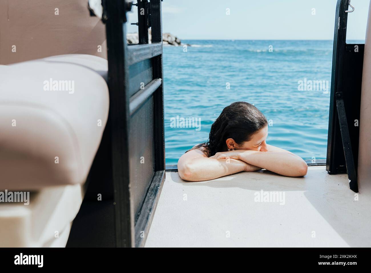 Dieses Bild fängt einen ruhigen Moment einer Frau ein, die sich während der Sommerferien am Meer entspannt. Sie wird gesehen, wie sie ihren Kopf auf ihren Armen ruht und die Ruhe genießt Stockfoto