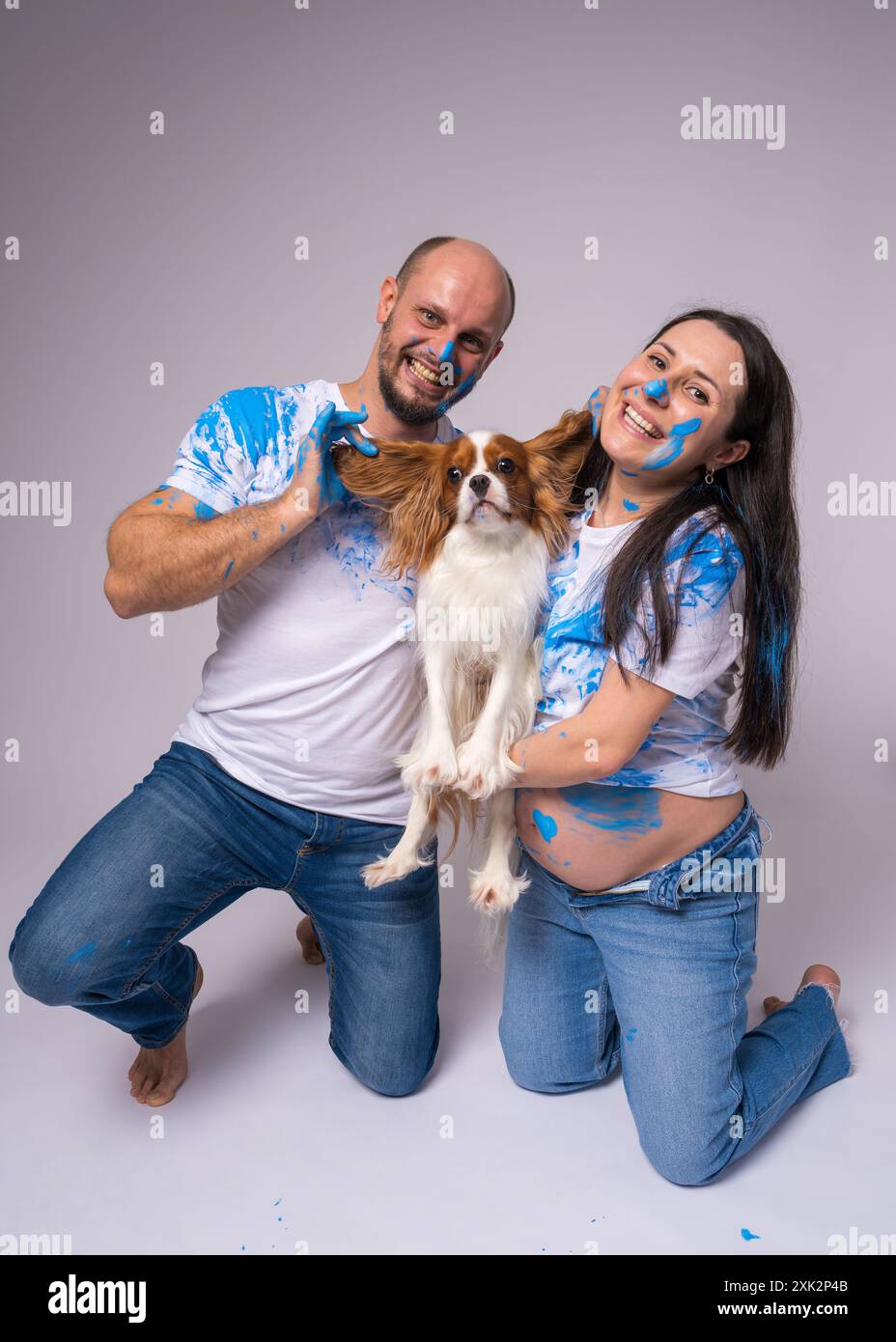 Ein Paar, ein Mann und eine schwangere Frau, die weiße T-Shirts tragen, die mit blauer Farbe befleckt sind, warten auf einen kleinen Jungen auf einer Gender-Enthüllungs-Party. Sie haben ein Do Stockfoto