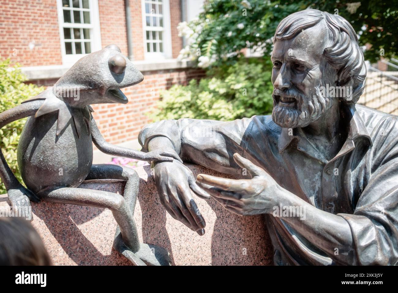 Jim Henson Memorial Kermit The Frog Statue College Park Maryland // COLLEGE PARK, Maryland, Vereinigte Staaten — das Jim Henson Memorial an der University of Maryland zeigt eine Bronzestatue des berühmten Puppenspielers mit seiner berühmten Schöpfung Kermit the Frog. Henson, ein Alumnus der Universität von Maryland, ist in entspannter Pose auf einer Bank zu sehen. Die Gedenkstätte außerhalb der Adele H. Stamp Student Union würdigt Hensons kreatives Erbe und seine Verbindung zur Universität. Stockfoto