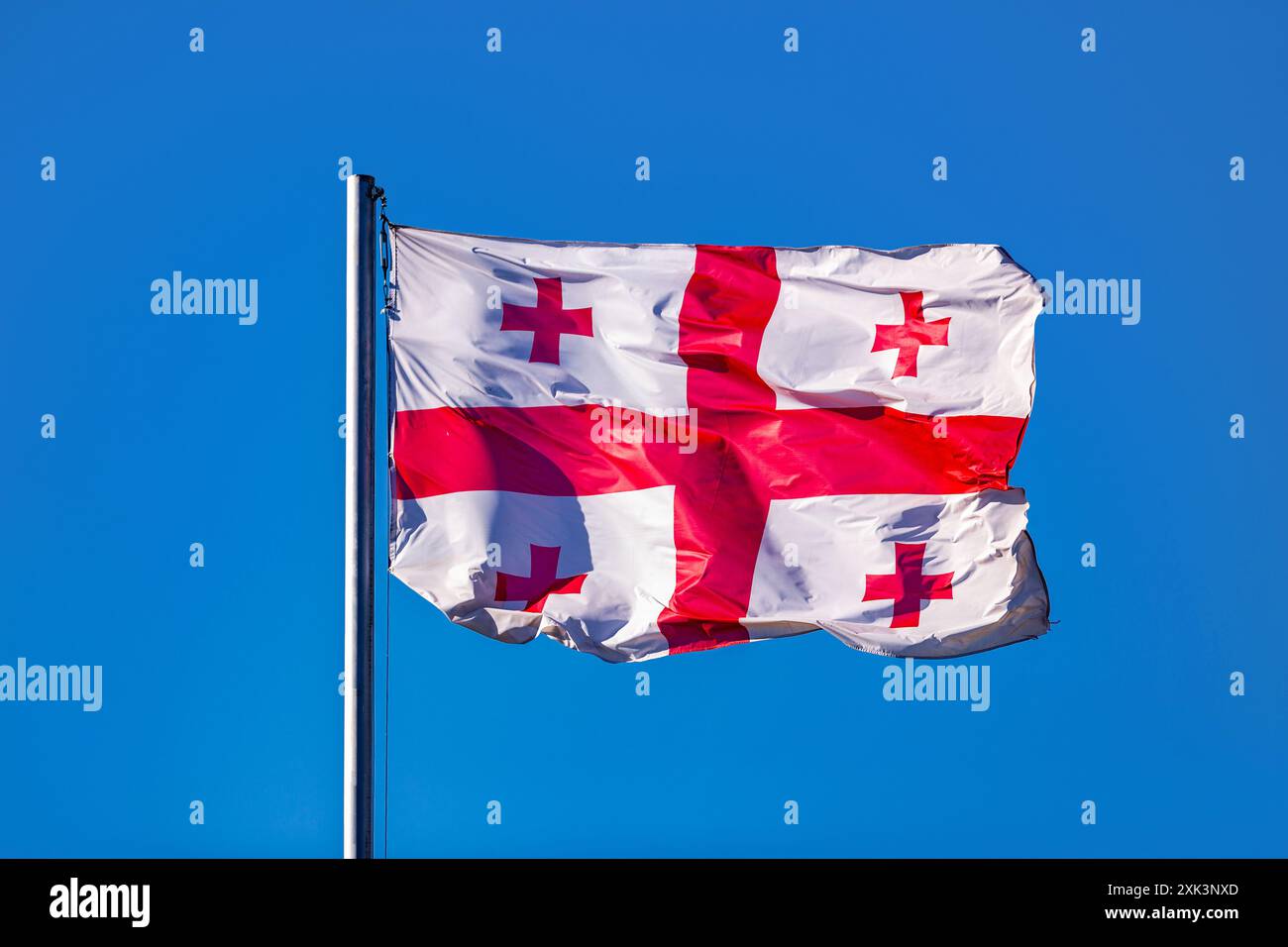 Große georgische Flagge auf einem Fahnenmast, die gegen den blauen Himmel winkt Stockfoto