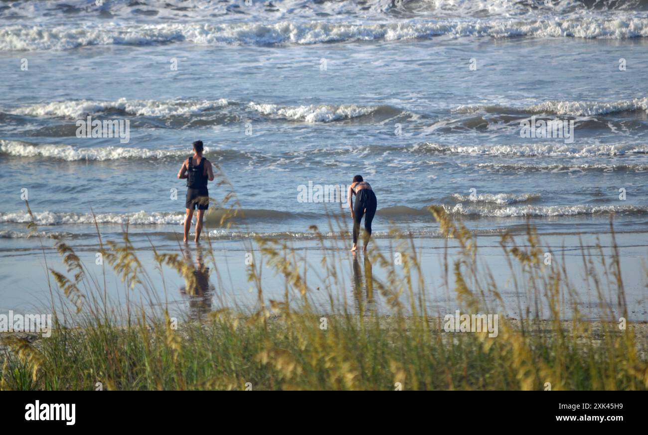 Ein junges Paar steht vor dem Meer, das eine steht hoch, während das andere umgebeugt ist. Beide fangen nach einem Morgenlauf auf North Myrtle Atem Stockfoto