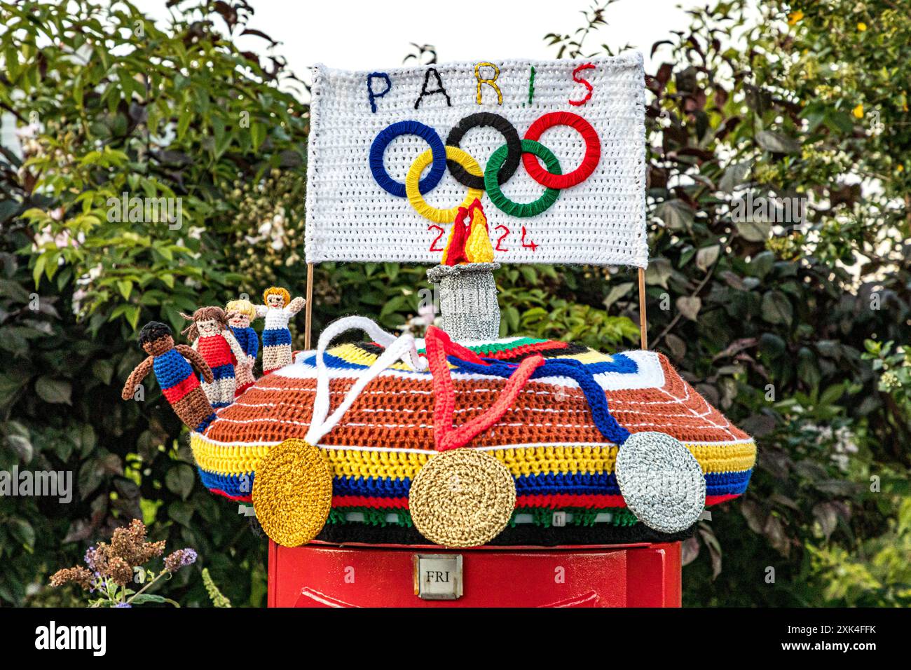 Farbenfrohe Strickkiste zur Feier der Olympischen Spiele 2024 in Paris mit Häkelmedaillen, Athleten, Flammen und Olympischen Ringen, Weymouth, Dorset Stockfoto