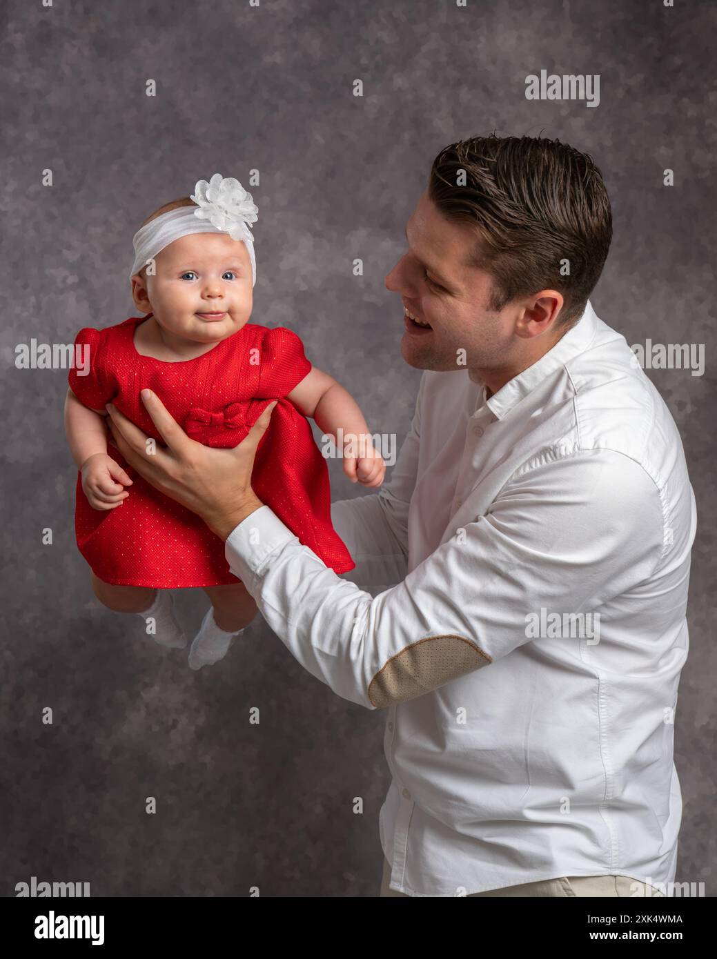 Glücklicher neuer Vater spielt mit süßem Baby, hebt, wirft niedliche Tochter in die Luft, hält das Baby mit Liebe in den Armen, lächelt, lacht, genießt Vaterschaft, Vater Stockfoto