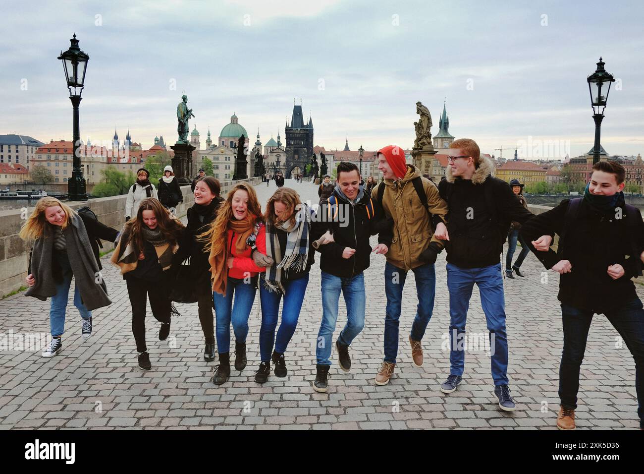 Eine Gruppe von Freunden verbindet ihre Arme zu einer menschlichen Kette der Freundschaft, glücklich und lachend über die Karlsbrücke in Prag am frühen Morgen Stockfoto