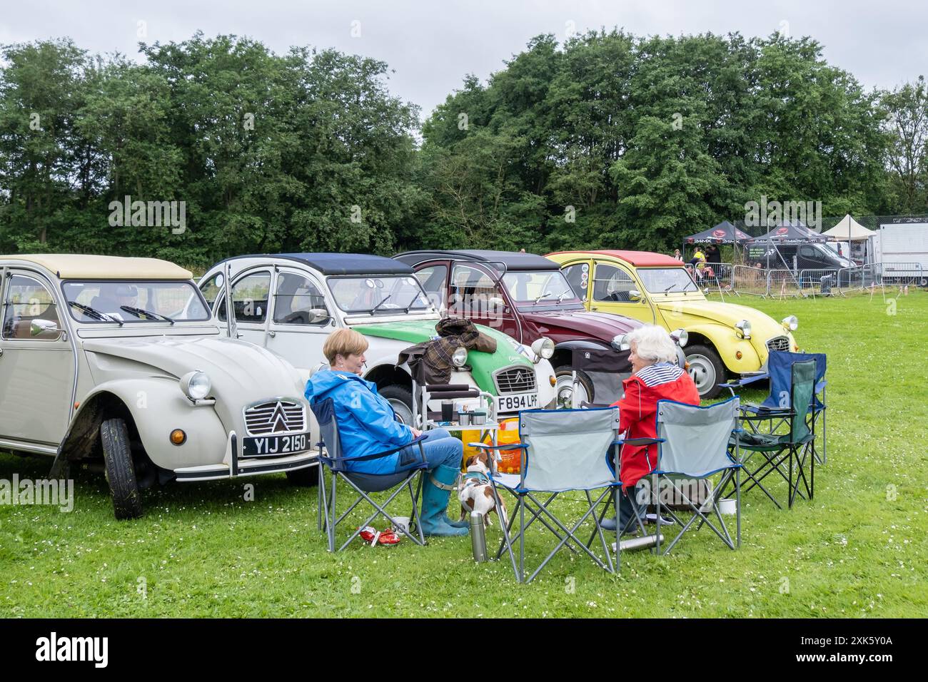 Ballymena, Nordirland - 20. Juli 2024: Damen sitzen vor einer Reihe klassischer französischer Citroen 2CV-Autos. Konzept Vintage, Chic, Retro, Motor Stockfoto
