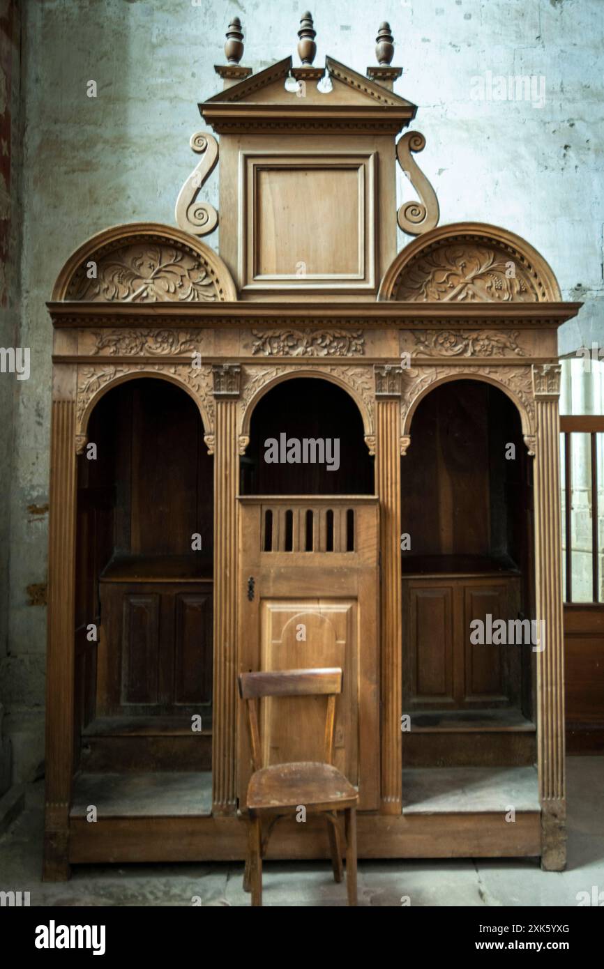 Aufwändig geschnitzter hölzerner Beichtstuhl im Kircheninnenraum in der Dämmerung. Frankreich Stockfoto