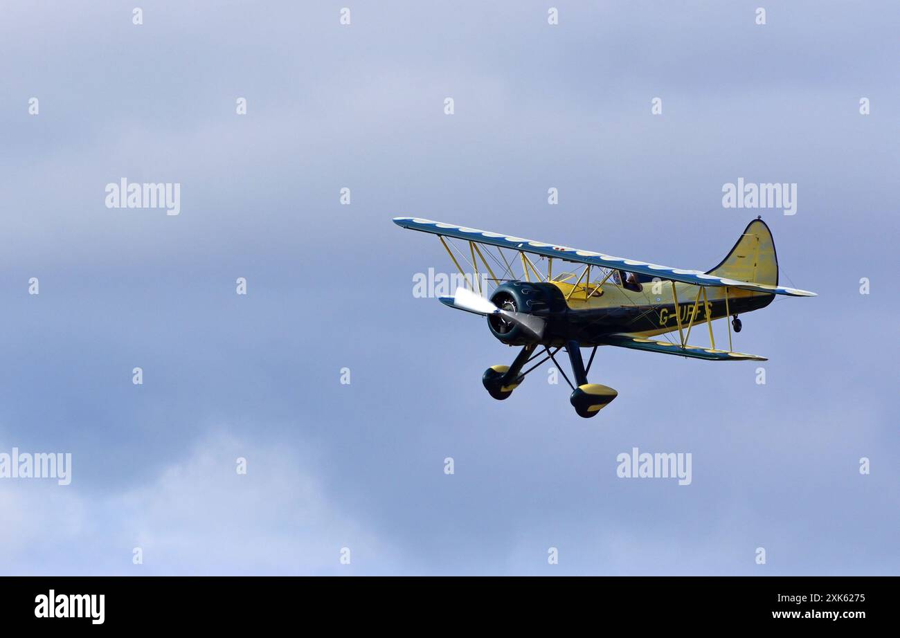 Vintage Waco UPF-7 Doppeldecker im Flug gegen Wolken. Stockfoto