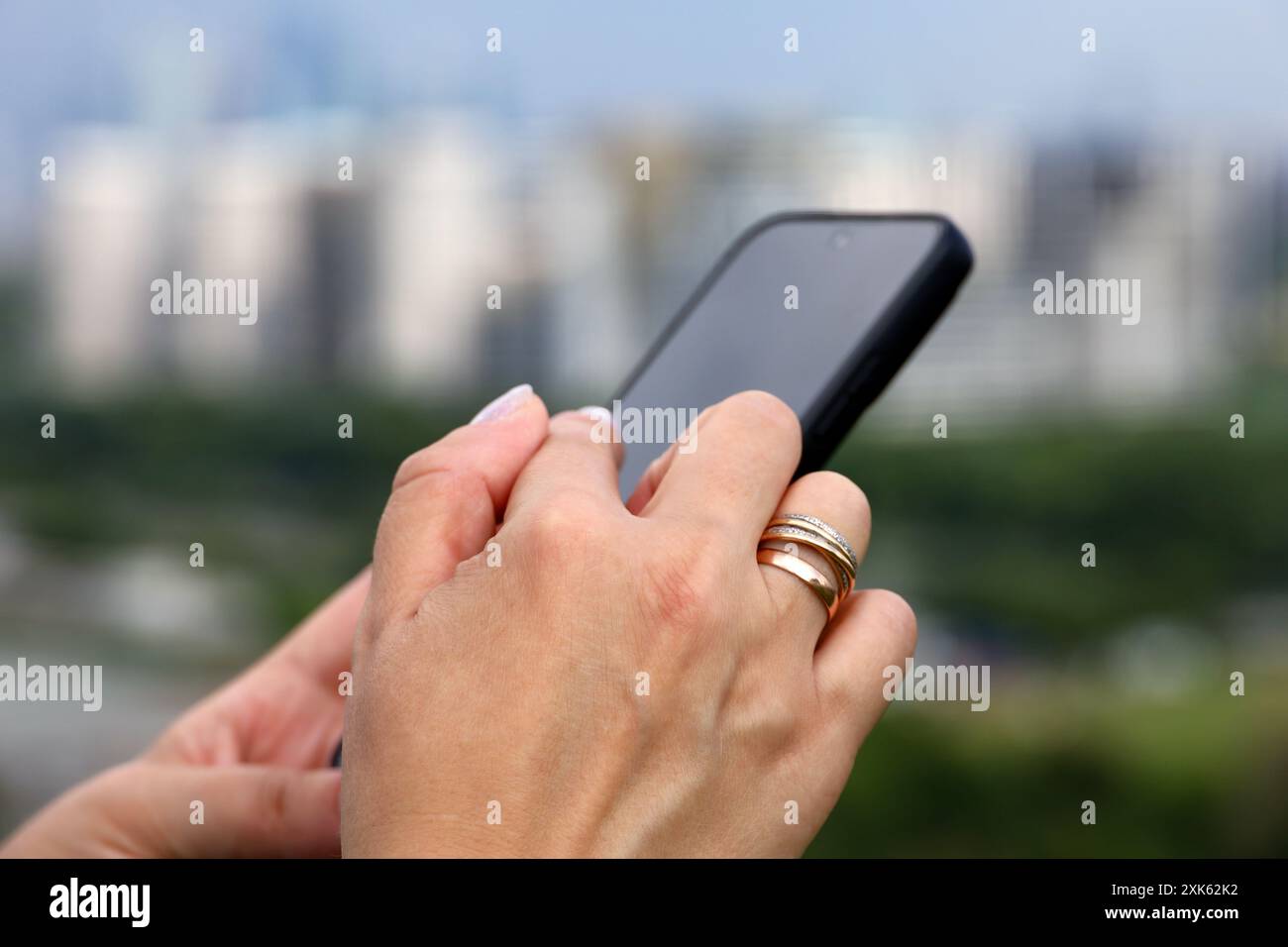 Weibliche Hände mit Smartphone nähern sich verschwommenem Hintergrund von Stadtgebäuden. Frau, die im Sommer das Handy benutzt Stockfoto