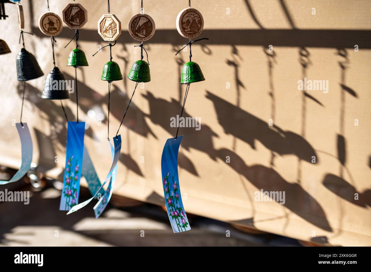 Eine Reihe farbenfroher Windspiele hängen im Sonnenlicht und werfen komplizierte Schatten auf eine Wand. Die Klingeltöne erzeugen ein optisch ansprechendes Muster mit ihrem V Stockfoto