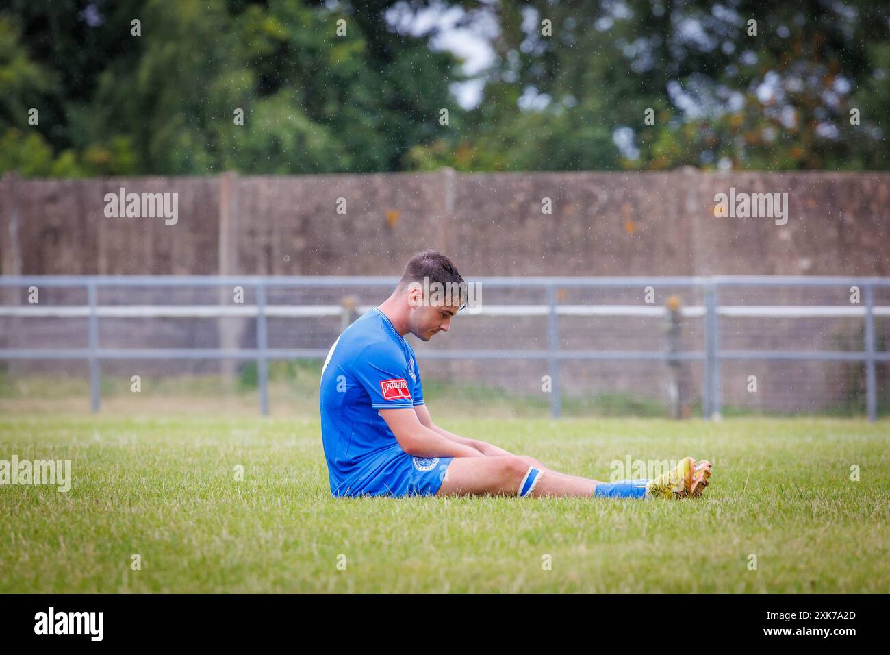 Der niederträchtige Fußballer sitzt allein auf dem Spielfeld und fühlt sich sehr deprimiert an Stockfoto