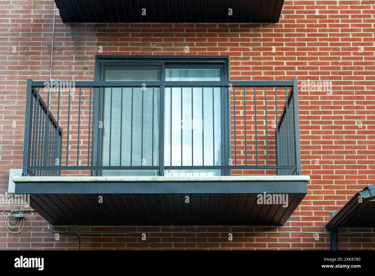 Die äußere rote Backsteinmauer eines Wohngebäudes. Der Balkon ist eines von mehreren Wohnungen mit grünen Metallgeländern und doppelten Glastüren. Stockfoto