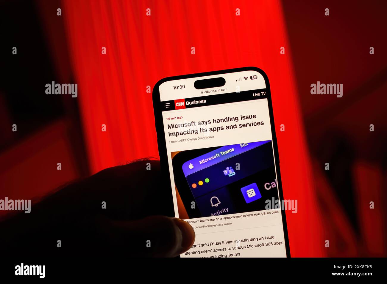 Paris, Frankreich - 20. Juli 2024: Aus Sicht des Blickwinkels hält eine männliche Hand ein iPhone und zeigt einen CNN Business-artikel über Microsoft, der Probleme behandelt, die sich auf seine Apps und Dienste auswirken, vor einem auffälligen roten Hintergrund Stockfoto