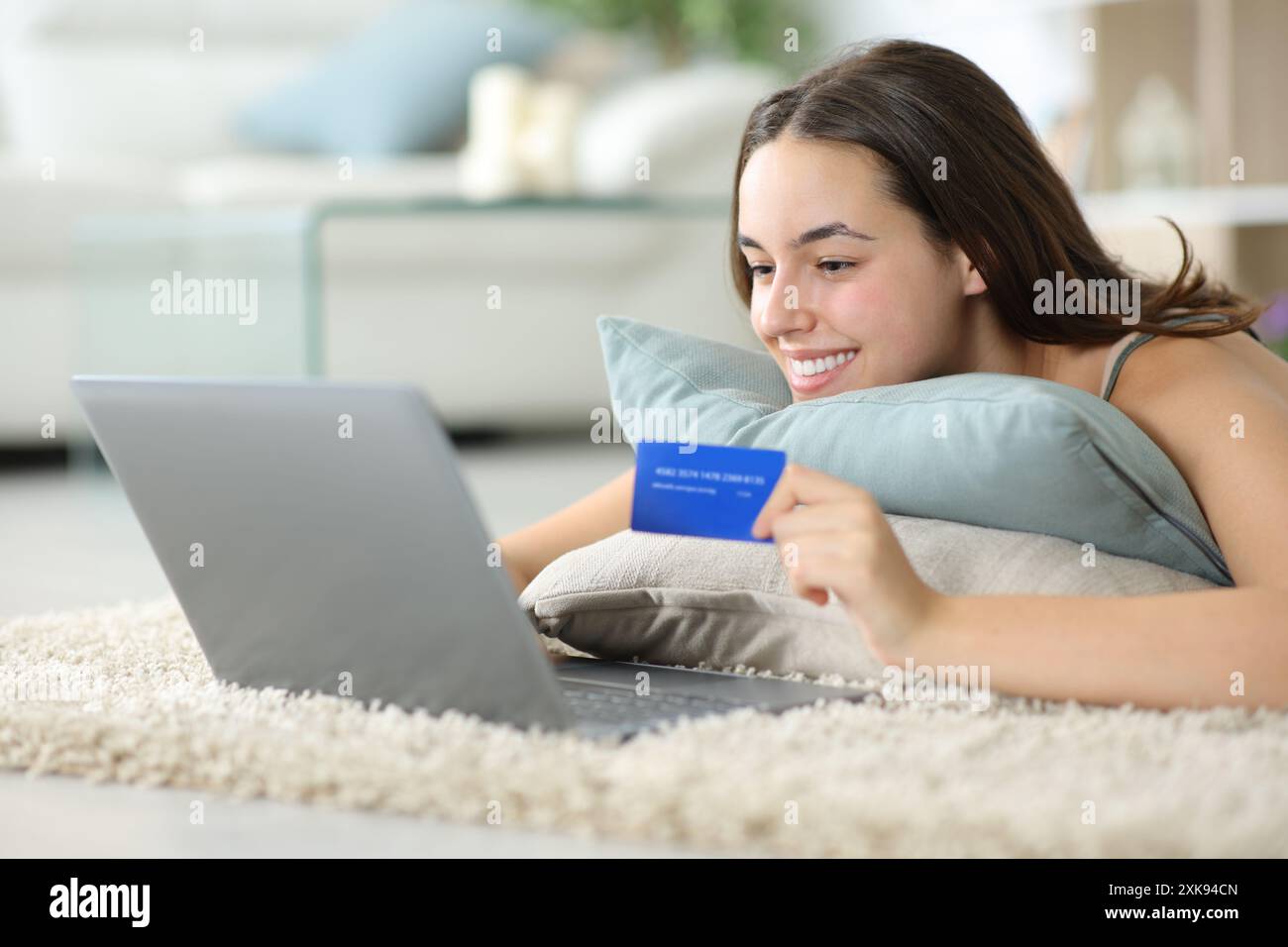 Glückliche Frau, die online mit Laptop und Kreditkarte zu Hause auf dem Boden kauft Stockfoto